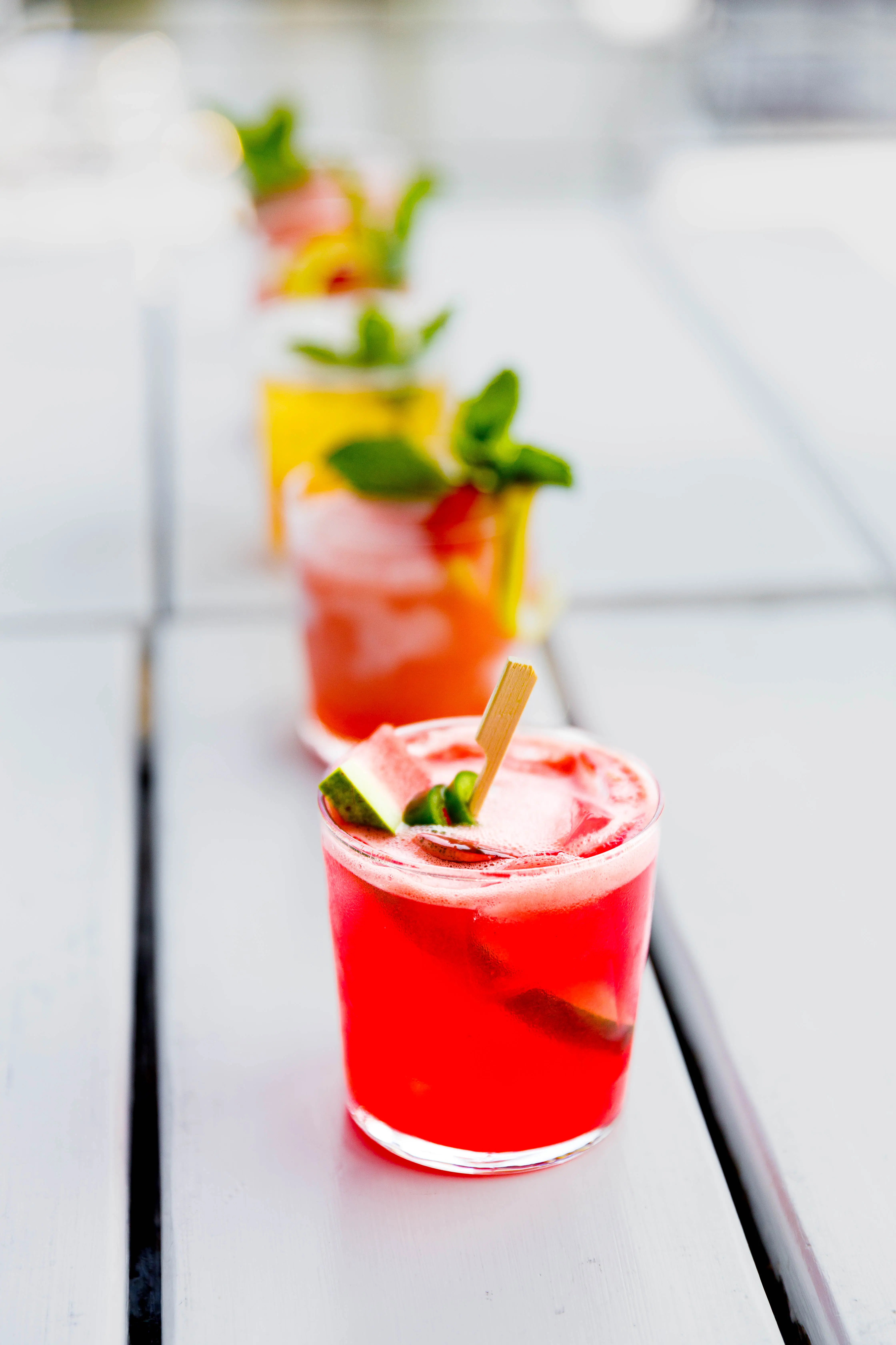 Two red cocktails garnished with watermelon and mint in soft daylight