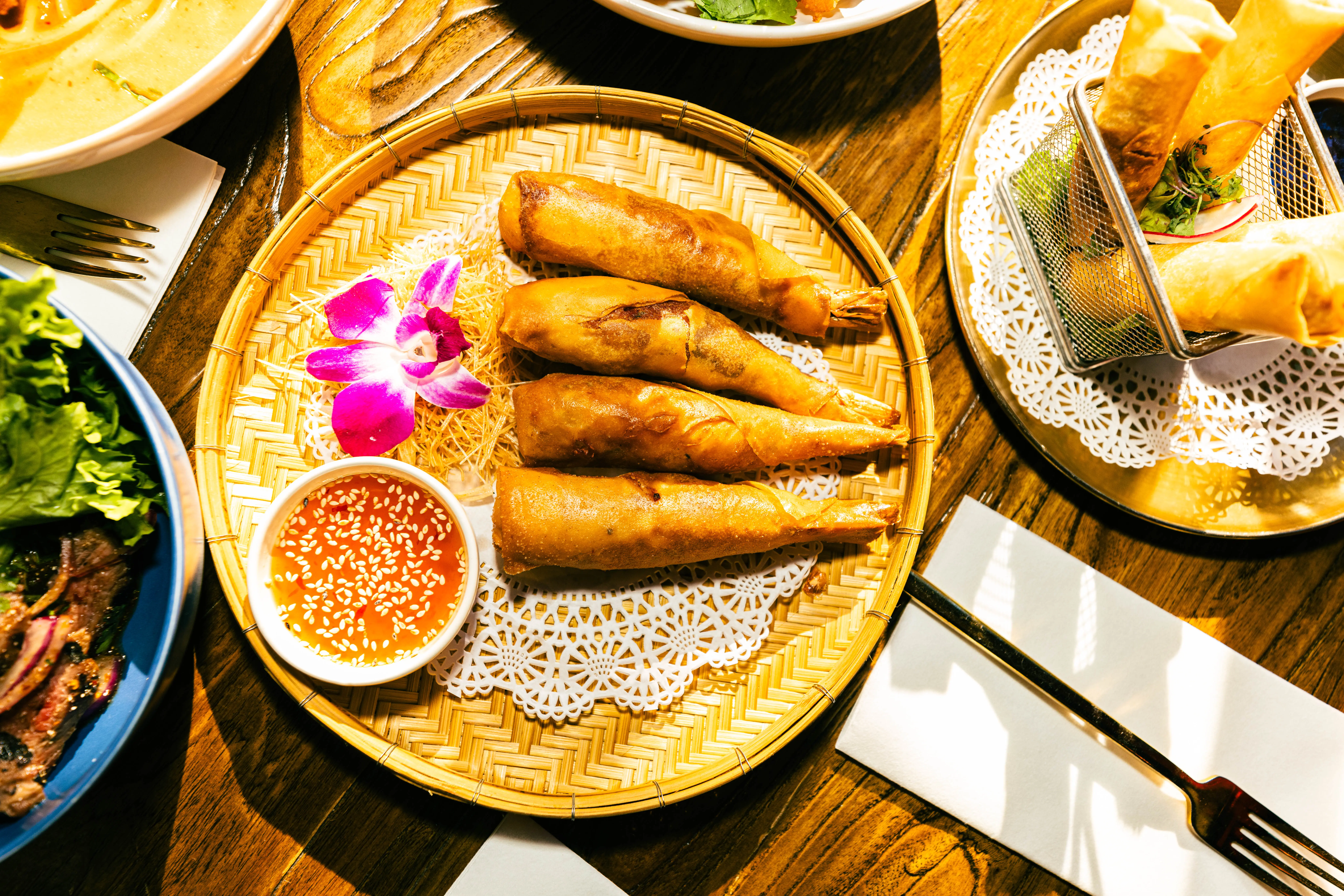 Golden fried spring rolls arranged on a woven tray with dipping sauce