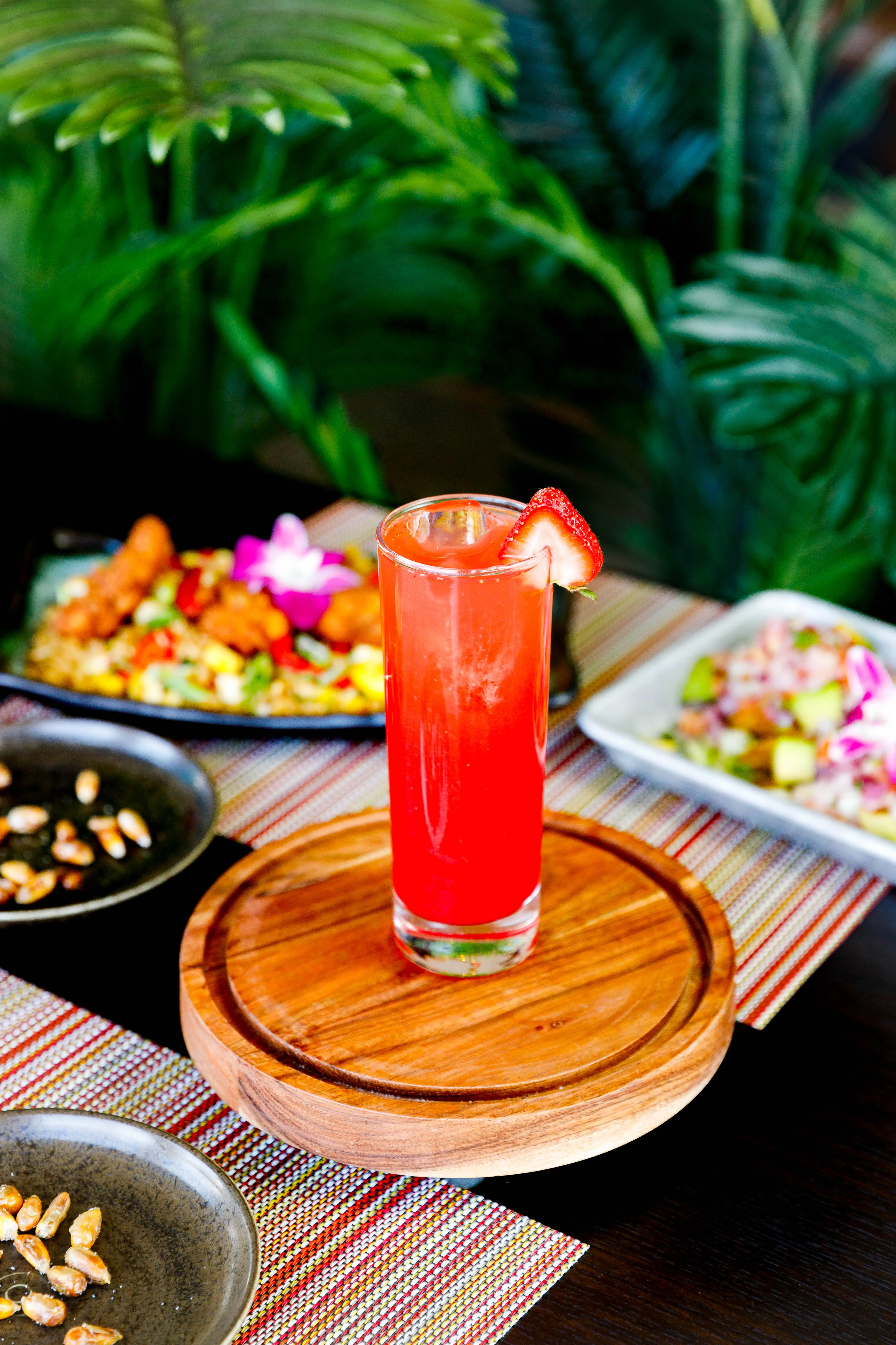Tall strawberry cocktail on a wooden board with plated dishes behind