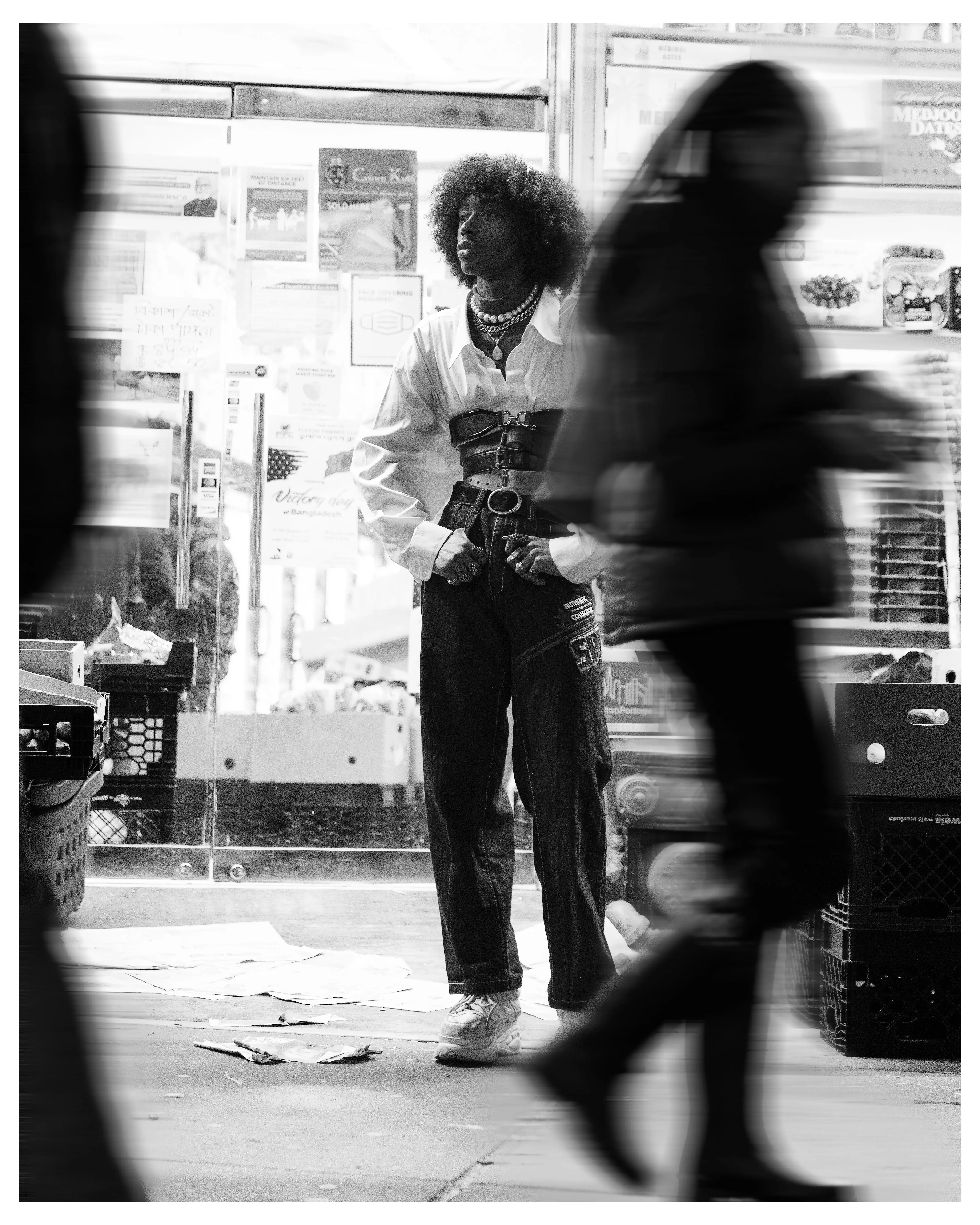 Black and white street portrait of a styled figure standing still as passersby blur past
