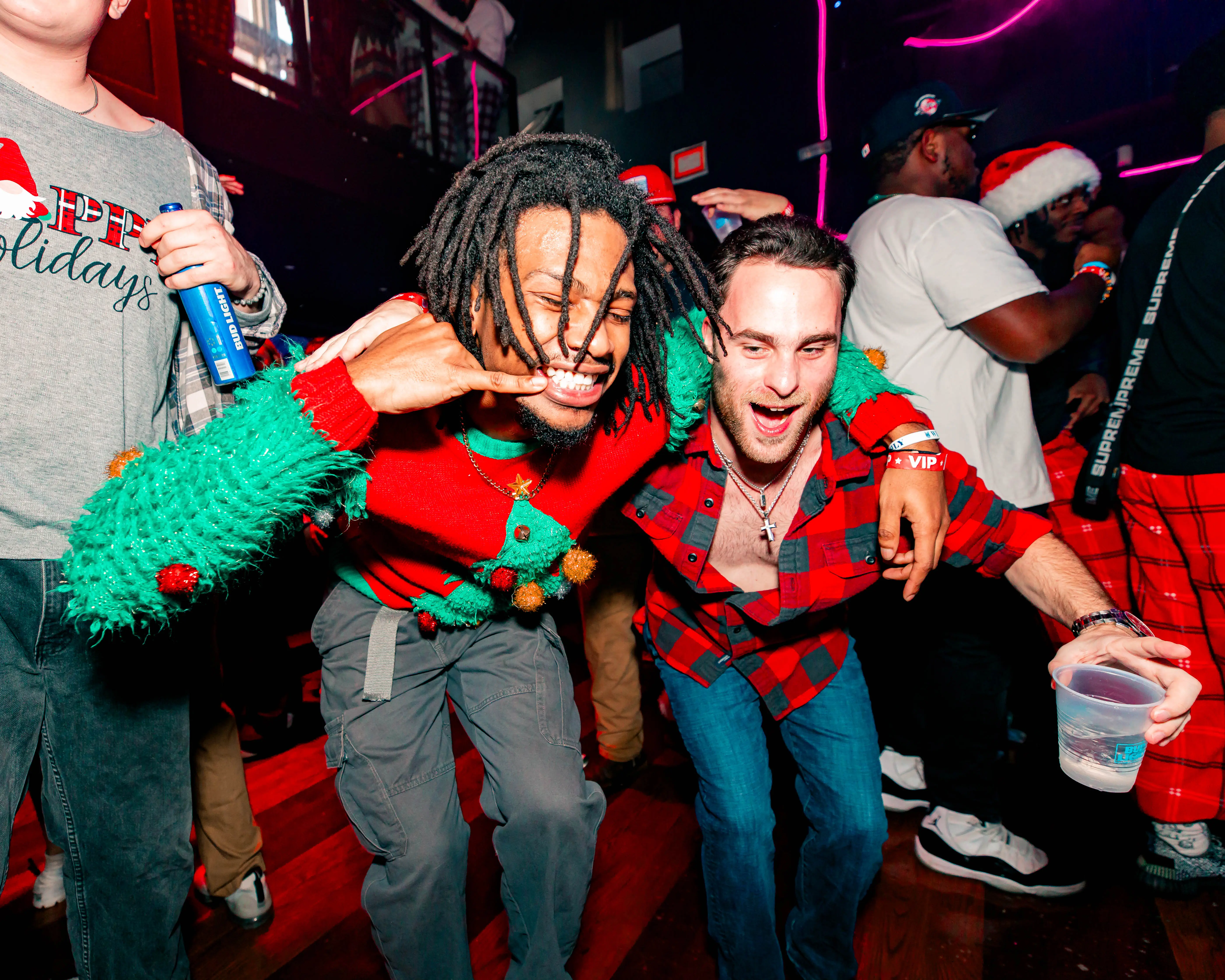 Two friends in holiday sweaters posing mid-laugh at an ugly-sweater party