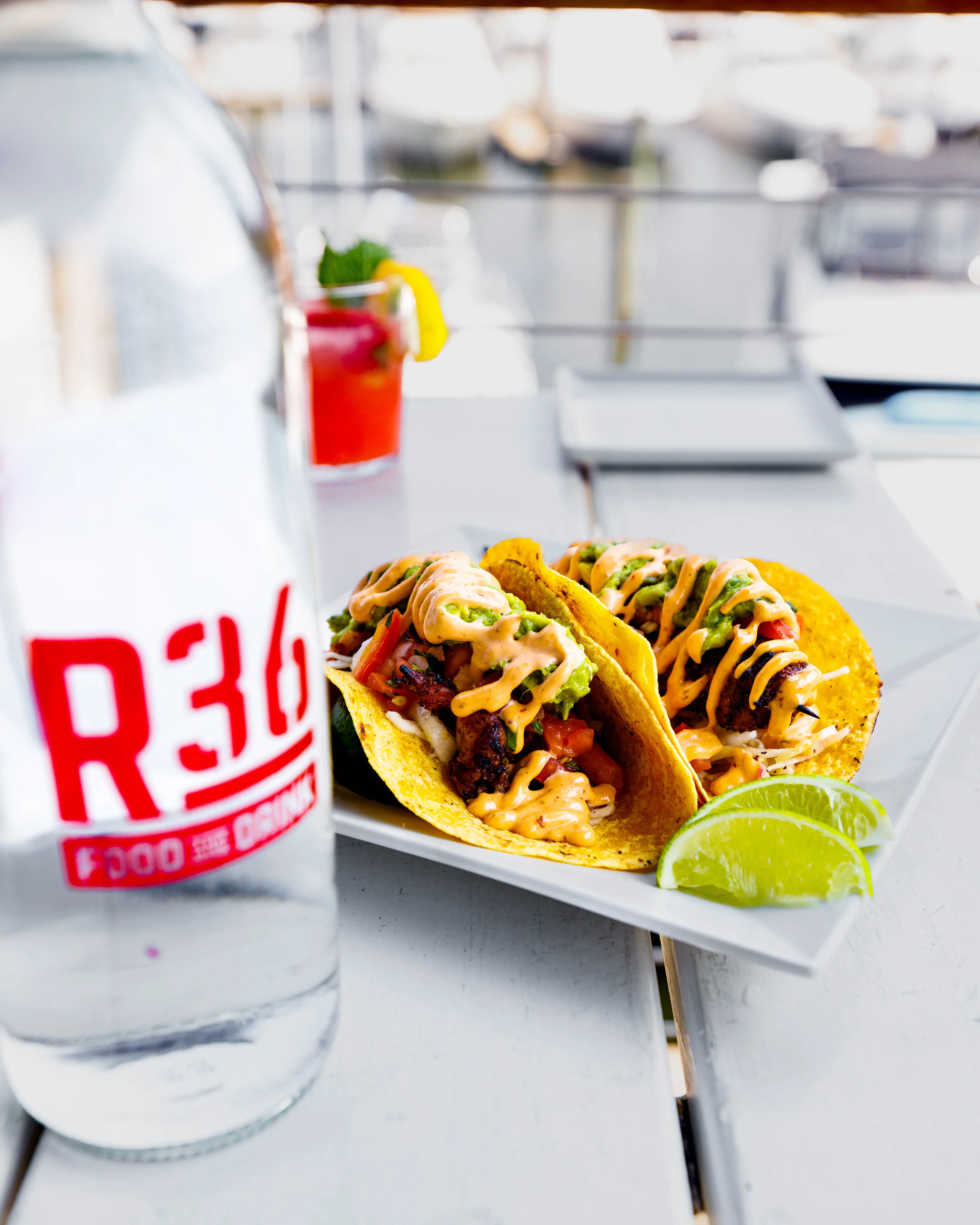 Three loaded tacos with lime wedges served on a white plate outdoors